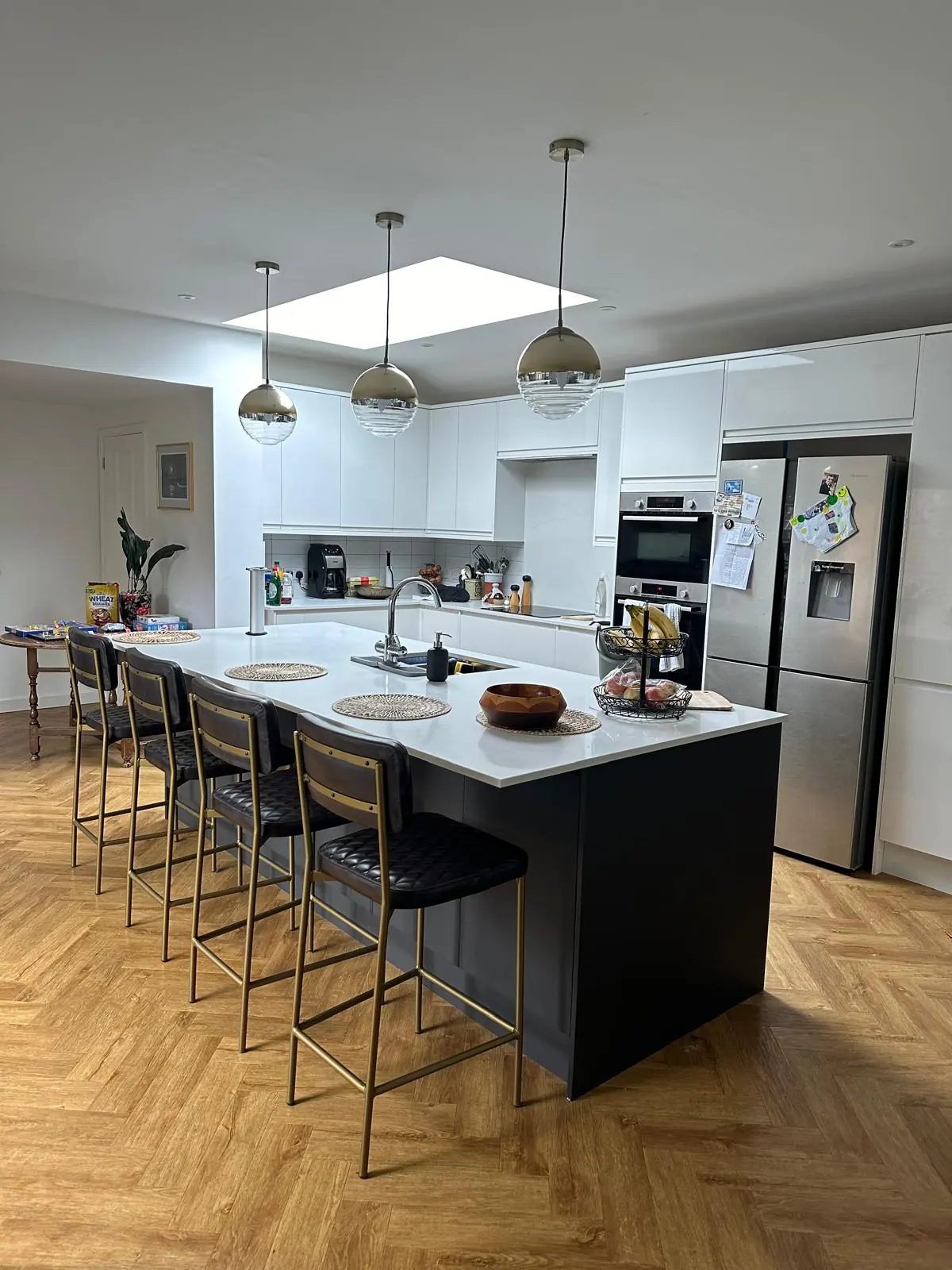 White kitchen with a dark island, pendant lights and herringbone flooring